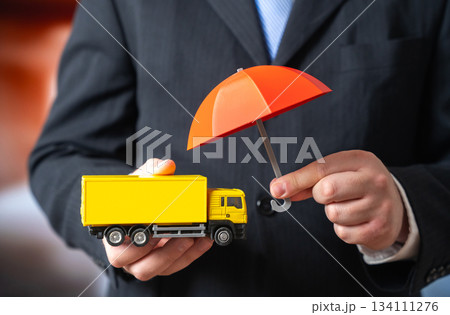 A businessman holds an umbrella over a truck. Concept for insurance of transportation and cargo. Logistics protection, supply chain risk management. Transport industry coverage and insurance promotion 134111276