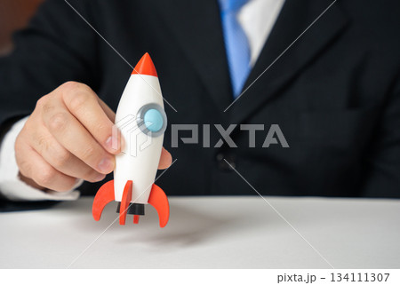 A businessman holds a startup rocket in his hand. Business launch. Innovation momentum and new project kickoff. Entrepreneurship content, startup ecosystems and investment inspiration. A businessman holds a startup rocket in his hand. Business launch. Innovation momentum and new project kickoff. Entrepreneurship content, startup ecosystems and investment inspiration. 134111307