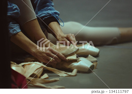 Closeup of hands preparing ballet shoes on studio floor 134111797