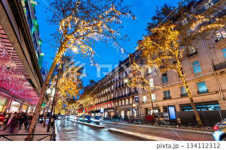 Golden Christmas lights illuminate trees along Boulevard Haussmann in Paris, France. Festive holiday decorations brighten the busy street near department stores at night Golden Christmas lights illuminate trees along Boulevard Haussmann in Paris, France. Festive holiday decorations brighten the busy street near department stores at night 134112312