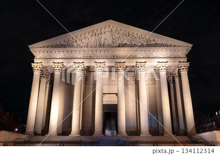 Illuminated La Madeleine church stands with Corinthian columns in Paris, France. Neoclassical Catholic temple features majestic stone facade and pediment sculpture under night sky 134112314