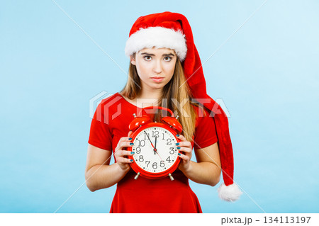 Sad woman wearing Santa costume holding clock 134113197