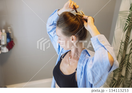 Woman meticulously ties her hair in bathroom mirror reflection 134113253