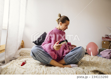 Young female gamer sitting peacefully in welllit bedroom environment Young female gamer sitting peacefully in welllit bedroom environment 134113260