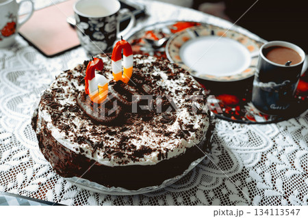 A chocolate cake with whipped cream and a candle with the number sixty on it sits on the table in the living room. 134113547