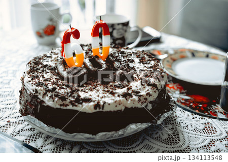 A chocolate cake with whipped cream and a candle with the number sixty on it sits on the table in the living room. 134113548