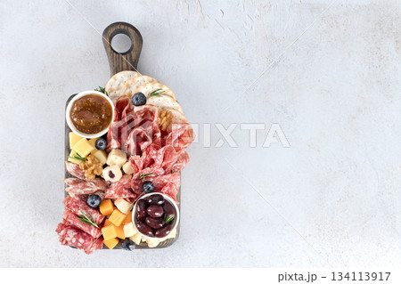 Charcuterie board with assorted meats, cheeses, olives, crackers and jam on white background. Top view. Copy space. Charcuterie board with assorted meats, cheeses, olives, crackers and jam on white background. Top view. Copy space. 134113917