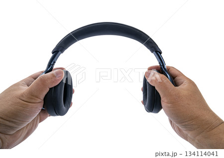 A pair of adult hands are holding black over-ear wireless headphones on a white background with a POV view, as if preparing A pair of adult hands are holding black over-ear wireless headphones on a white background with a POV view, as if preparing 134114041
