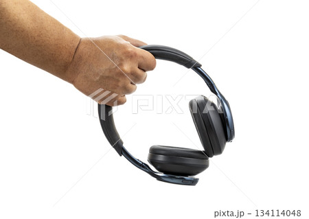 A hand holding black wireless over-ear headphones with cushioned ear pads against a white background in a close-up view. A hand holding black wireless over-ear headphones with cushioned ear pads against a white background in a close-up view. 134114048