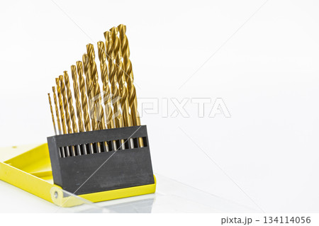 Set of gold-colored drill bits arranged in ascending size order in a yellow plastic case on a white background showing precision Set of gold-colored drill bits arranged in ascending size order in a yellow plastic case on a white background showing precision 134114056