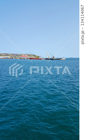 Turquoise Pacific bay with calm, crystalline waters; two ships anchored by a distant island harbor. 134114067