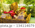 Wicker basket with assorted Christmas gifts, bright pouches, festive decorations under tree branches. Holiday surprise, seasonal magic, joyful celebration. Blurred Christmas background, postcard 134114079