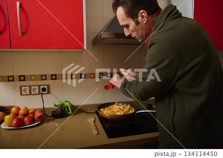 Man Cooking Potatoes On Stove In Modern Kitchen With Red Cabinets 134114450