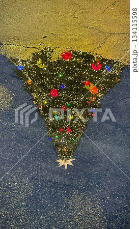 Bright reflection of a decorated Christmas tree in a puddle on dark urban asphalt pavement at night Bright reflection of a decorated Christmas tree in a puddle on dark urban asphalt pavement at night 134115598