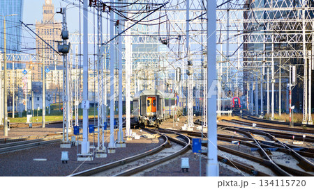 Warsaw, Poland. 28 November 2025. A passenger train on the tracks near the station. Tracks, electrical wires and metal masts against the backdrop of a city skyscrapers on a winter day. Warsaw, Poland. 28 November 2025. A passenger train on the tracks near the station. Tracks, electrical wires and metal masts against the backdrop of a city skyscrapers on a winter day. 134115720