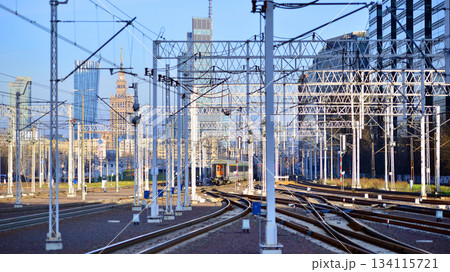 Warsaw, Poland. 28 November 2025. A passenger train on the tracks near the station. Tracks, electrical wires and metal masts against the backdrop of a city skyscrapers on a winter day.  134115721