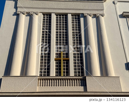 Church facade with tall columns and golden cross under clear sky. Religious heritage, spiritual architecture, solemn atmosphere and timeless cultural significance. Church facade with tall columns and golden cross under clear sky. Religious heritage, spiritual architecture, solemn atmosphere and timeless cultural significance. 134116123