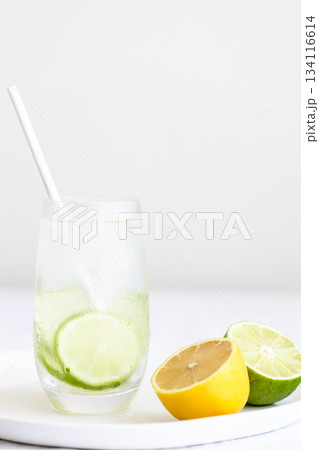Glass of cold lime water with paper straw and halfs of lime and lemon. 134116614