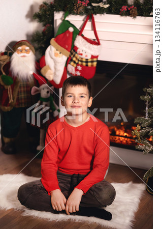 Young boy celebrating christmas holiday by fireplace at home Young boy celebrating christmas holiday by fireplace at home 134116763