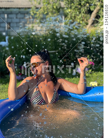 Woman relaxing in inflatable pool splashing water in backyard garden Woman relaxing in inflatable pool splashing water in backyard garden 134116810