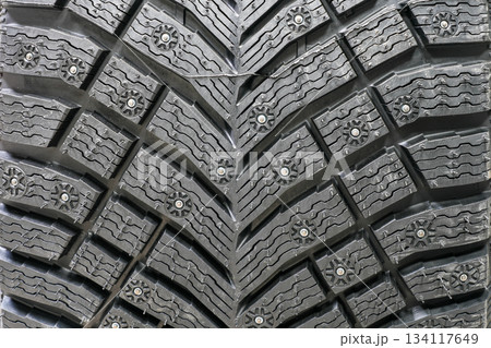 Studded winter tire tread pattern showing deep grooves and metal studs for icy road traction 134117649