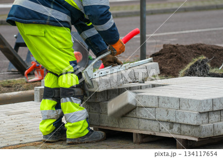 Road worker lifting concrete paving blocks with tool during construction of sidewalk on urban street Road worker lifting concrete paving blocks with tool during construction of sidewalk on urban street 134117654
