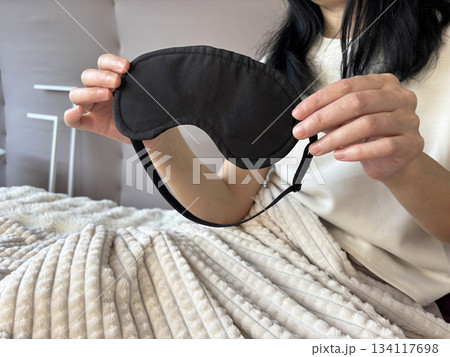 Adult brunette woman sitting in bed with a sleep mask after a good night sleep, cozy morning routine, healthy sleep, wellness and self care lifestyle	 134117698