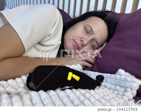 Sleeping adult woman with sleep mask and earplugs beside her, concept of peaceful rest and noise protection Sleeping adult woman with sleep mask and earplugs beside her, concept of peaceful rest and noise protection 134117703