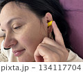 Close up of adult brunette woman inserting yellow earplugs, noise protection for healthy sleep, deep rest, insomnia prevention and peaceful home bedroom atmosphere 134117704