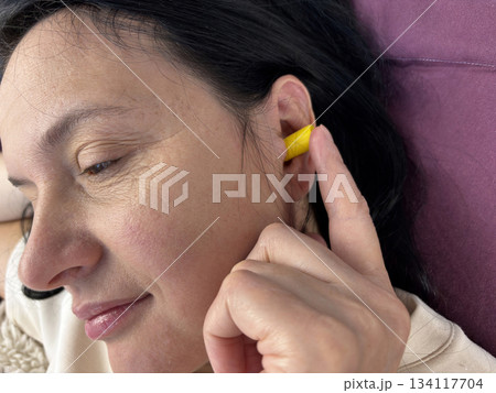 Close up of adult brunette woman inserting yellow earplugs, noise protection for healthy sleep, deep rest, insomnia prevention and peaceful home bedroom atmosphere 134117704