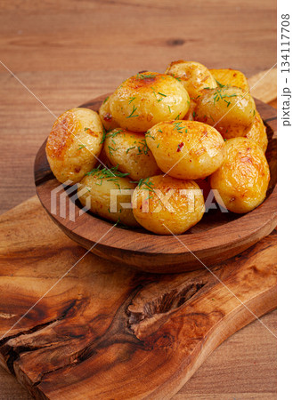 Baked new potatoes, with butter and dill, on a wooden plate, homely, rustic, no people, Baked new potatoes, with butter and dill, on a wooden plate, homely, rustic, no people, 134117708