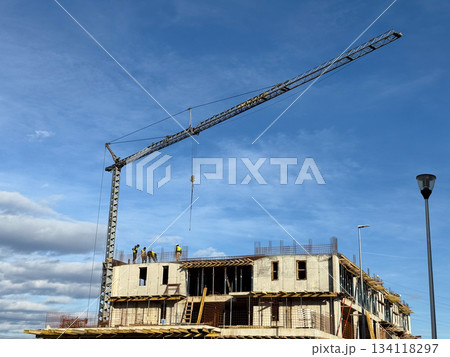 Construction site with workers on unfinished concrete building under crane arm. Urban development, industry, labor and modern city growth. Construction site with workers on unfinished concrete building under crane arm. Urban development, industry, labor and modern city growth. 134118297