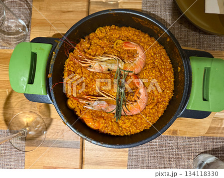 Paella with shrimp served in pan on wooden table. Rich seafood flavor, warm dinner mood, rustic homemade meal and cozy Mediterranean dining atmosphere 134118330