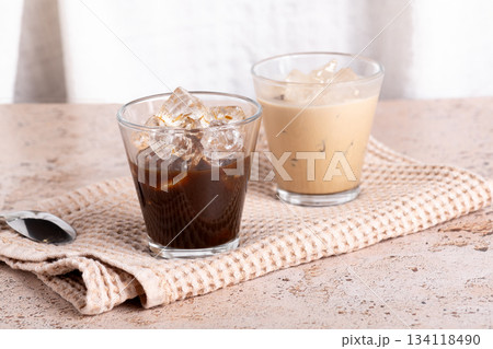 Iced coffee and black coffee served in clear glasses on beige stone table 134118490