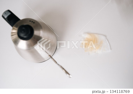 High-angle view of electric kettle pouring steaming water into drip coffee maker, coffee-stained napkin nearby highlighting potential kitchen mishap on clean white surface, close-up, nobody. High-angle view of electric kettle pouring steaming water into drip coffee maker, coffee-stained napkin nearby highlighting potential kitchen mishap on clean white surface, close-up, nobody. 134118769
