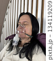 Adult woman using a home nebulizer inhaler while sitting in a cozy bedroom, respiratory treatment at home for breathing relief, healthcare and medical therapy concept, realistic lifestyle scene 134119209