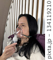 Adult woman using a home nebulizer inhaler while sitting in a cozy bedroom, respiratory treatment at home for breathing relief, healthcare and medical therapy concept, realistic lifestyle scene 134119210
