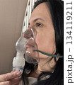 Adult woman using a home nebulizer inhaler while sitting in a cozy bedroom, respiratory treatment at home for breathing relief, healthcare and medical therapy concept, realistic lifestyle scene 134119211