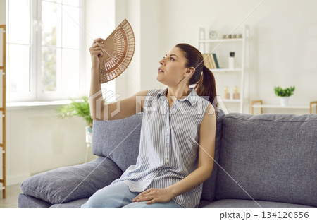 Stressed tired woman using fan suffering from heat, summer high temperature at home. 134120656