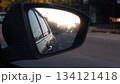 Side mirror view of black car. Close up on side car reflection in the mirror. With blurred of car driving on clear road with sunlight on the town faraway . Environment of evening time. 134121418
