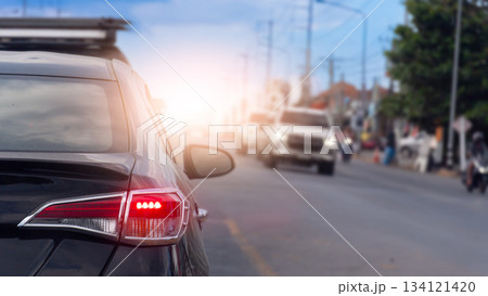Rear side of black car with turn on brake light. Close up tail light of car with bright light of the brake lights. Blurred of other car on opposite road. With environment of city in the country. Rear side of black car with turn on brake light. Close up tail light of car with bright light of the brake lights. Blurred of other car on opposite road. With environment of city in the country. 134121420