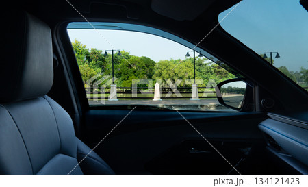 Interior on car close up on the seat and console inside of car. Can view landscape of side road with steel fence and forest under clear sky. Interior on car close up on the seat and console inside of car. Can view landscape of side road with steel fence and forest under clear sky. 134121423