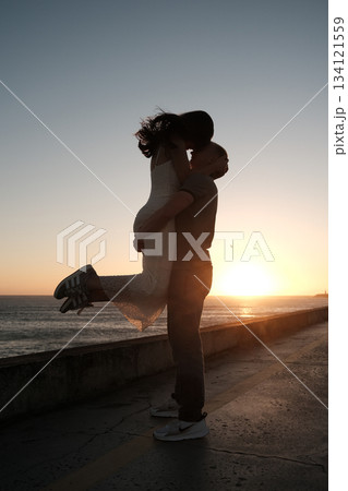 Man lifting woman in joyful embrace by the sea at sunset, romantic silhouette moment filled with love and happiness. Man lifting woman in joyful embrace by the sea at sunset, romantic silhouette moment filled with love and happiness. 134121559