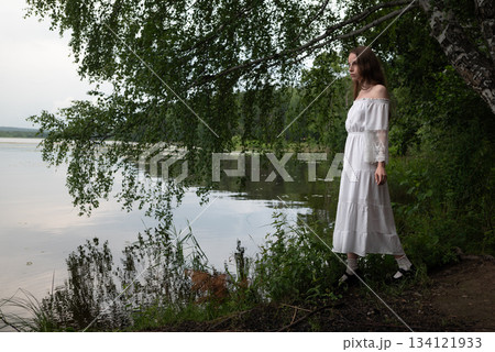 Elegance by the Lake: Woman in White Off-Shoulder Dress Among Birch Trees Elegance by the Lake: Woman in White Off-Shoulder Dress Among Birch Trees 134121933