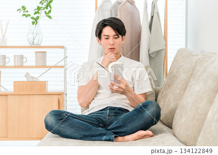 リビングのソファーに座り読書する若いアジア人男性 リビングのソファーに座り読書する若いアジア人男性 134122849