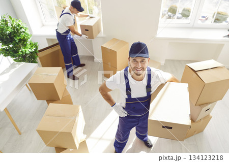 Portrait of moving service worker packing and carrying cardboard boxes with colleague. Portrait of moving service worker packing and carrying cardboard boxes with colleague. 134123218