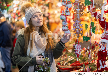 Young woman in souvenir store examines Christmas cloth toys and figurines Young woman in souvenir store examines Christmas cloth toys and figurines 134124293