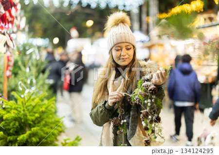 Girl looks at garland made of fir cones and brunchs, Xmas atmosphere Girl looks at garland made of fir cones and brunchs, Xmas atmosphere 134124295