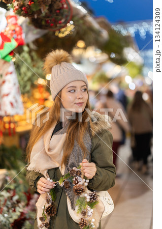 Girl with cone and fir brunch garland stands in middle fair decorated for New Year holidays 134124309