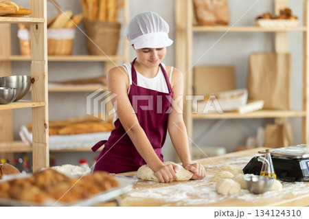 Teen girl works in bakery as baker, kneads dough, works with flour. 134124310